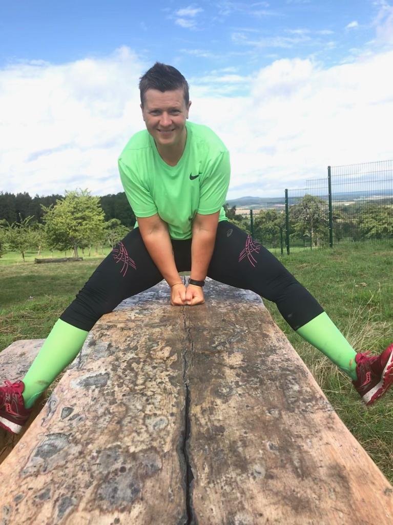 Katja hockt auf einem Baumstamm am Feldrand und lacht in die Kamera