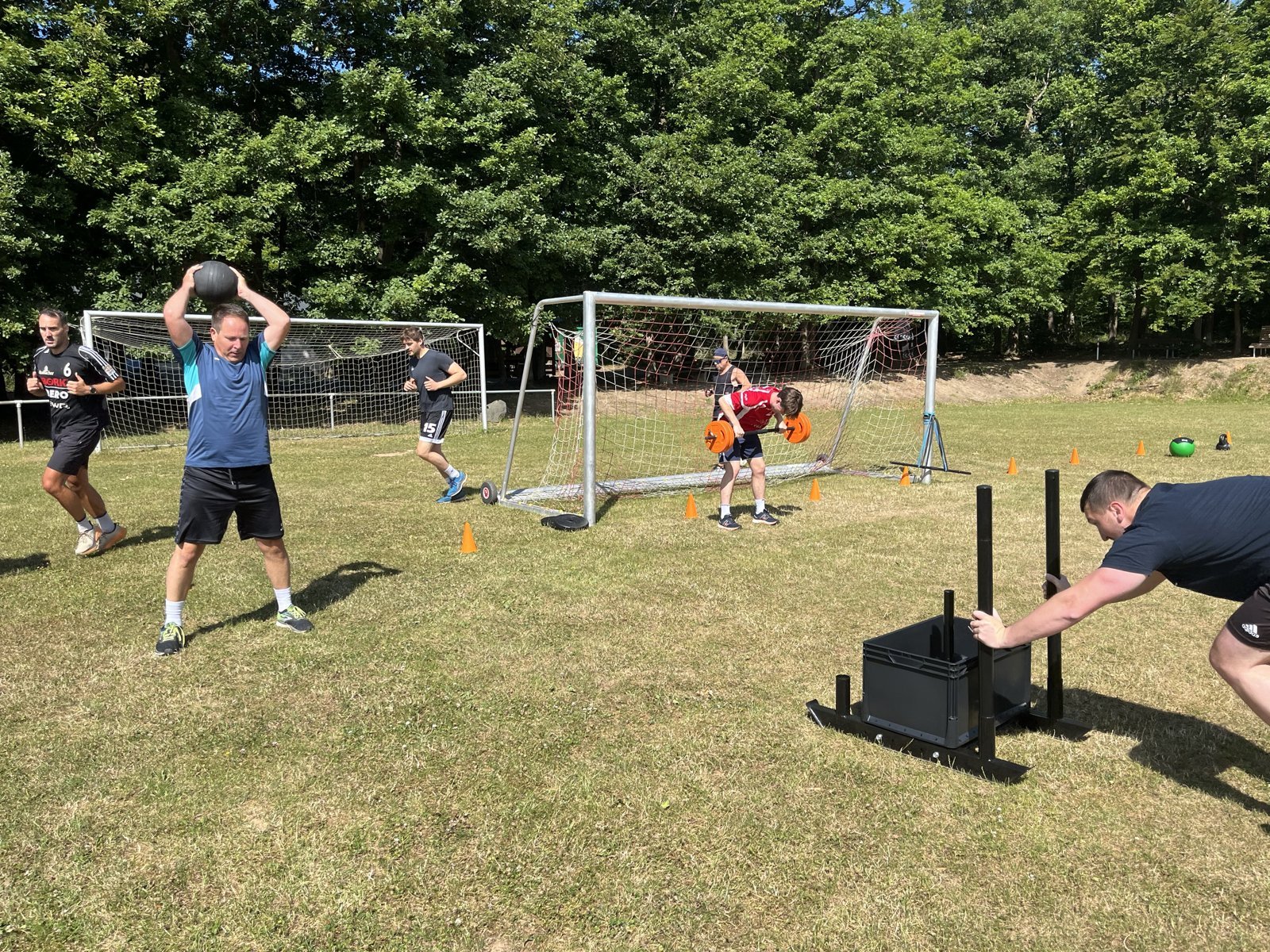 Teamtraining auf dem Sportplatz: Schlitten schieben und Medizinball über dem Kopf