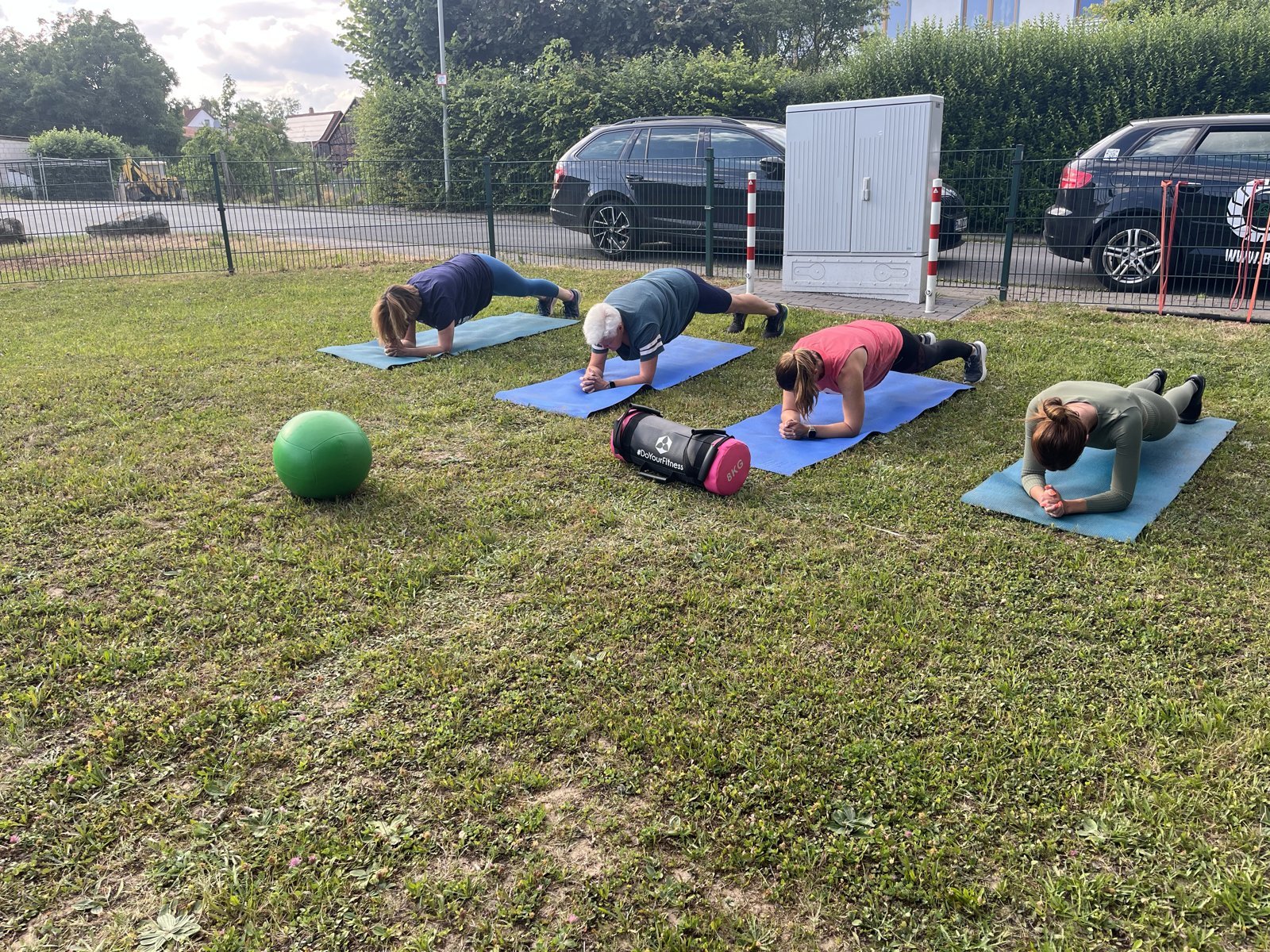 Vier Teilnehmende halten die Plank auf Matten, grüner Medizinball im Vordergrund