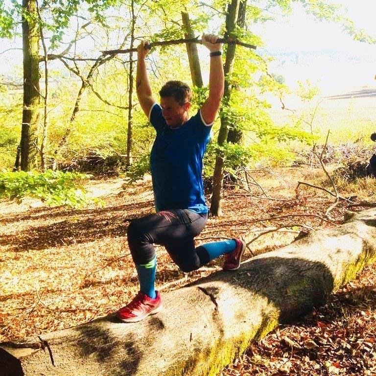 Katja im Herbstwald im Ausfallschritt auf einem Baumstamm, Stock über dem Kopf