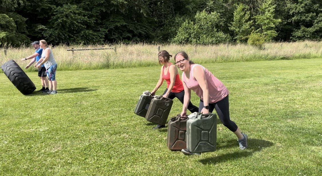 Zwei Frauen tragen Kanister über die Wiese, Reifen im Hintergrund